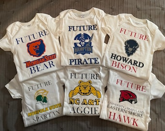 May include: White baby vests with the word "FUTURE" printed above college team logos. The logos include a bear, a pirate, a bison, a bulldog, a hawk, and a Spartan. The vests are made of soft fabric.