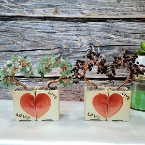 May include: Two wire-wrapped gemstone trees in ceramic pots with heart-shaped designs. The trees are made with green and brown gemstones and the pots have the word "Love" written on them.