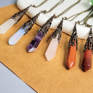 Op de afbeelding: Zes kristallen punt hangers aan delicate kettingen met sierlijke bronzen instellingen. De kristallen zijn helder, opaal, amethist, rozenkwarts, rode jaspis en carneol.