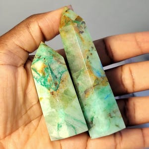 May include: Two polished crystal points with a hexagonal shape. The stones feature a translucent light green base color with prominent inclusions of vibrant teal, deep forest green, and warm golden-brown mineral veins throughout the surfaces.