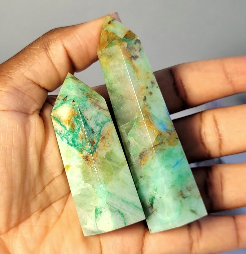 May include: Two polished crystal points with a hexagonal shape. The stones feature a translucent light green base color with prominent inclusions of vibrant teal, deep forest green, and warm golden-brown mineral veins throughout the surfaces.