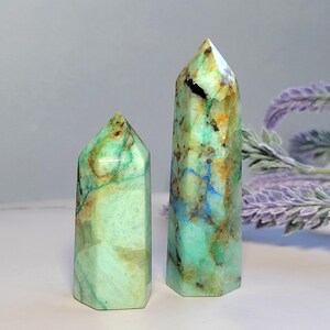 May include: Two polished crystal towers with a hexagonal base and pointed top. The stones feature a light green base color with prominent veins of brown, tan, and bright blue mineral inclusions throughout the smooth, semi-translucent surfaces.