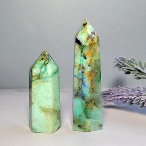 May include: Two polished crystal towers with hexagonal points. The stones feature a marbled appearance with vibrant shades of mint green, golden yellow, deep blue veins, and small black inclusions throughout the smooth, translucent surfaces.