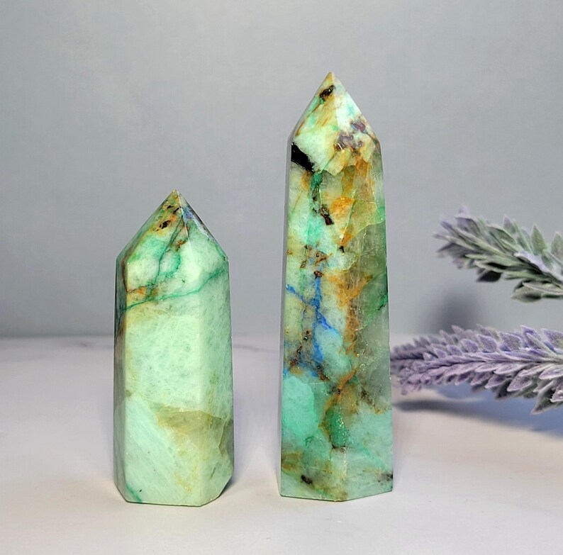 May include: Two polished crystal towers with hexagonal points. The stones feature a marbled appearance with vibrant shades of mint green, golden yellow, deep blue veins, and small black inclusions throughout the smooth, translucent surfaces.