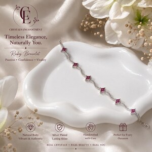 May include: A silver-toned chain bracelet featuring five evenly spaced, square-shaped red ruby gemstones. The bracelet is displayed on a white, wavy-edged ceramic dish. Text on the image includes Crystals Enchantment, Timeless Elegance, Naturally You, and Ruby Bracelet, along with icons for natural ruby, silver plated, handcrafted, and gift-ready features.