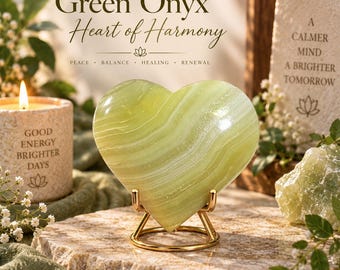 May include: A polished light green onyx stone carved into a heart shape, resting on a gold-toned metal display stand. The stone features natural white banding and a smooth, glossy finish, centered in a display with candles and stone signage.