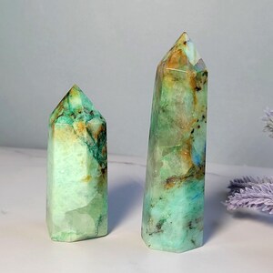 May include: Two polished crystal towers with a hexagonal base and pointed top. The stones feature a marbled appearance with shades of mint green, teal, and brown inclusions, displaying a translucent quality with natural internal fractures.