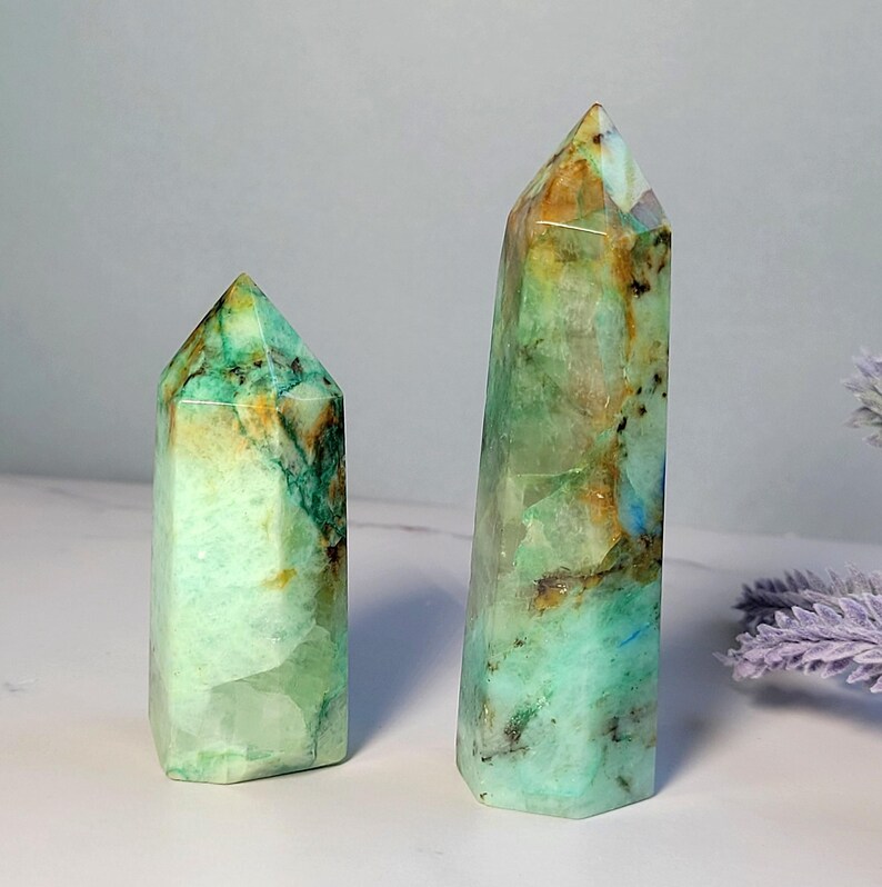 May include: Two polished crystal towers with a hexagonal base and pointed top. The stones feature a marbled appearance with shades of mint green, teal, and brown inclusions, displaying a translucent quality with natural internal fractures.