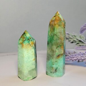 May include: Two polished crystal towers with hexagonal bases. The stones feature a marbled appearance with vibrant shades of mint green, teal, and patches of warm golden-brown. The surfaces are smooth with visible internal fractures and inclusions.