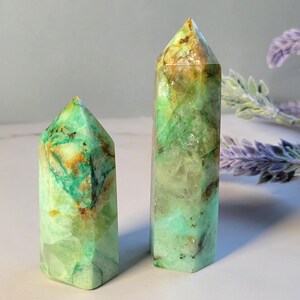 May include: Two polished crystal points with a hexagonal shape. The stones feature a vibrant mix of translucent mint green, opaque teal, and warm amber-colored inclusions throughout their faceted surfaces, ending in a sharp, pointed apex.