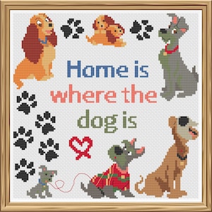 Könnte beinhalten: Kreuzstich-Kunstwerk in einem Holzrahmen mit verschiedenen Hundeillustrationen und dem Text "Home is where the dog is". Die Hunde sind in Braun-, Grau- und Beigetönen gehalten, mit Pfotenabdrücken und einem roten Herz.