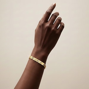 Peut inclure: Un bracelet doré avec un motif unique de lignes et de formes. Le bracelet est porté au poignet, et l'arrière-plan est de couleur neutre.