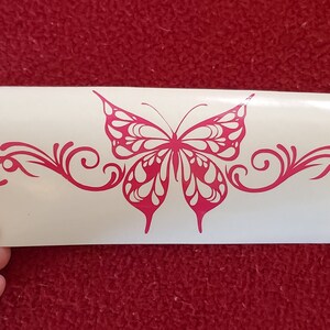 May include: Pink butterfly decal with a decorative swirl design. The butterfly has white accents and is centered on a white background.