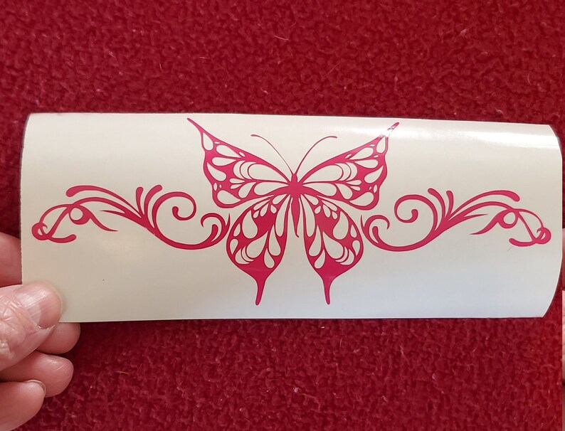 May include: Pink butterfly decal with a decorative swirl design. The butterfly has white accents and is centered on a white background.