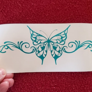 May include: Teal blue butterfly decal with ornate scrollwork on either side. The butterfly has a detailed design with white accents.