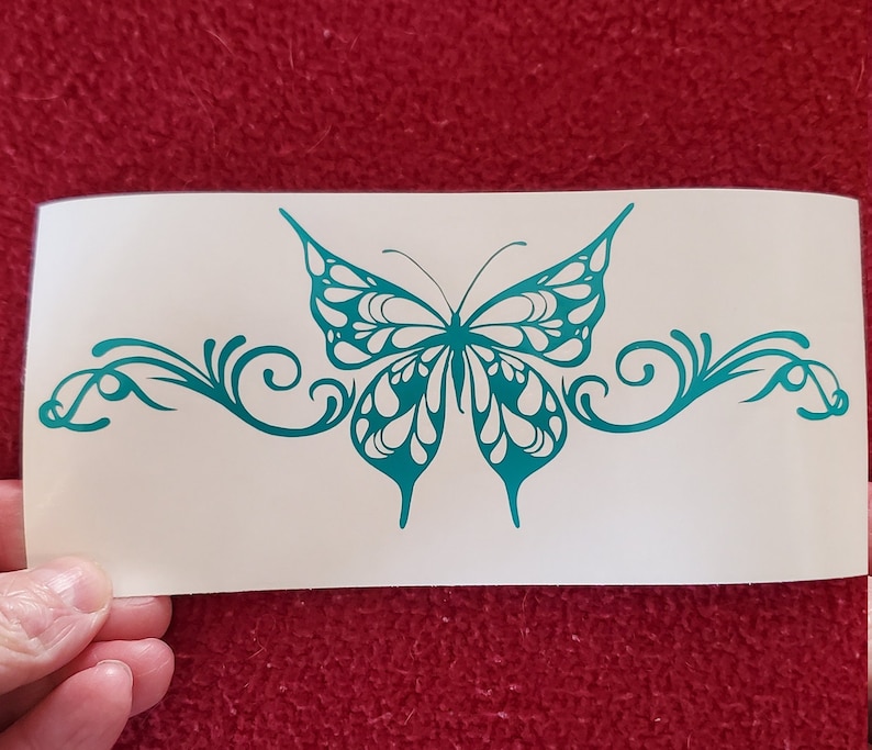 May include: Teal blue butterfly decal with ornate scrollwork on either side. The butterfly has a detailed design with white accents.