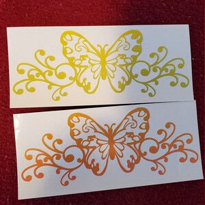 Puede incluir: Dos hojas blancas de papel con un dise&ntilde;o de mariposa amarilla y naranja. La mariposa est&aacute; rodeada de un dise&ntilde;o floral decorativo. La mariposa y el dise&ntilde;o floral est&aacute;n recortados en el papel.
