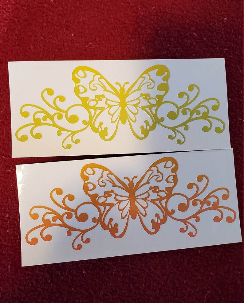 Puede incluir: Dos hojas blancas de papel con un dise&ntilde;o de mariposa amarilla y naranja. La mariposa est&aacute; rodeada de un dise&ntilde;o floral decorativo. La mariposa y el dise&ntilde;o floral est&aacute;n recortados en el papel.