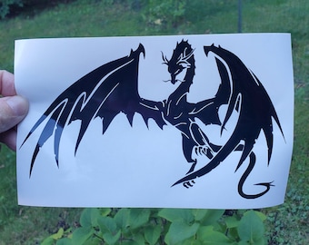 May include: A black dragon sticker with detailed wings, a long tail, and a dynamic pose. The dragon is shown against a white background. The sticker is designed to be applied to a surface.