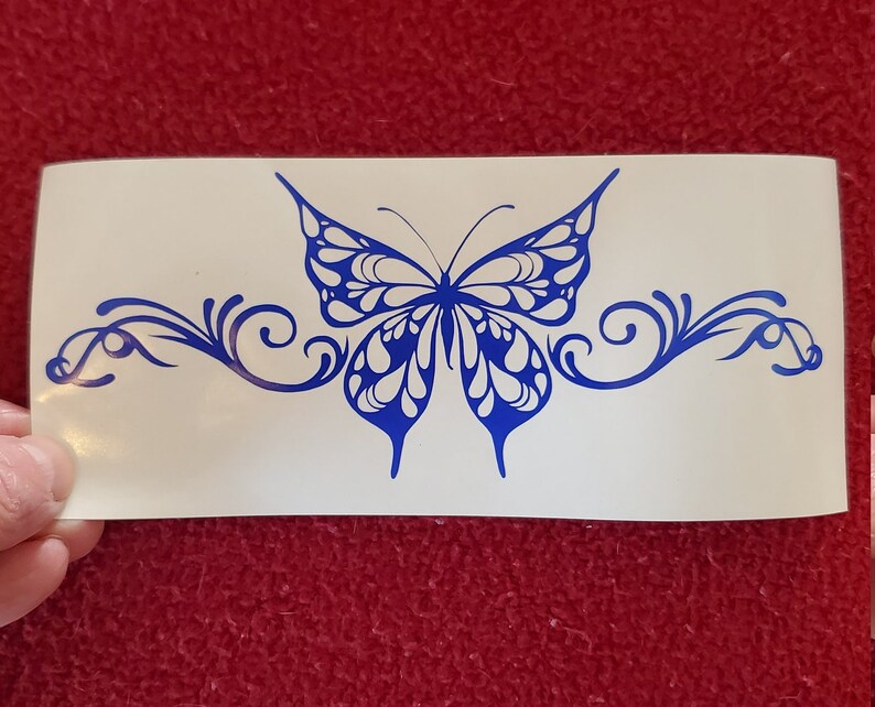 May include: A blue butterfly with intricate wing patterns is centered on a white background. The butterfly is surrounded by a decorative, swirling design.