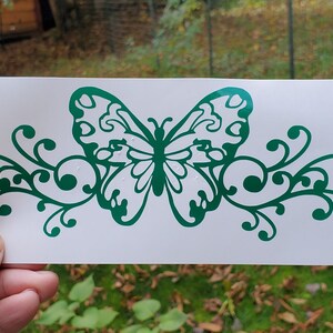 Puede incluir: Calcoman&iacute;a de vinilo verde de una mariposa con acentos florales en espiral. La mariposa tiene un dise&ntilde;o detallado con alas intrincadas.