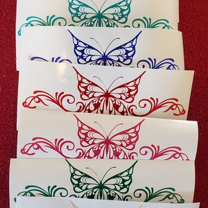 May include: Set of seven butterfly decals in various colors, including purple, teal, blue, red, pink, green, and yellow. Each decal features a stylized butterfly with intricate details and a swirling floral design.