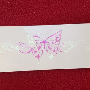 May include: A white vinyl decal with a pink butterfly design. The butterfly has intricate details and is surrounded by a decorative scrollwork design.