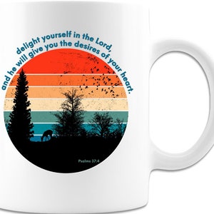 May include: White ceramic mug with a vintage sunset design featuring a deer, trees, and birds. The mug has the text "delight yourself in the Lord, and he will give you the desires of your heart. Psalms 37:4" printed on it.