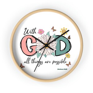 May include: A white round clock with a wood frame. The clock face features a floral design with butterflies and a sun. The text "With God all things are possible" is written in black script with the Bible verse "Matthew 19:26" below.