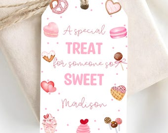Puede incluir: Una etiqueta de regalo rectangular blanca con un agujero y cordel, decorada con puntos rosas e ilustraciones de dulces que incluyen un pretzel, macaron, cupcake y corazones. El texto dice: A special TREAT for someone so SWEET Madison.