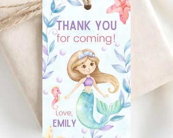 Puede incluir: Una etiqueta de regalo rectangular con un agujero y cordel, con una ilustración en acuarela de una sirena, un caballito de mar, estrellas de mar y algas. El texto dice: THANK YOU for coming! Love, EMILY. Fondo azul claro con burbujas.