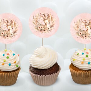 Könnte beinhalten: Drei Cupcakes mit weißem Frosting und bunten Streuseln, die mit runden rosa und braunen Kuchen-Toppern verziert sind, die ein Cartoon-Reh mit einem Blumenkranz zeigen.