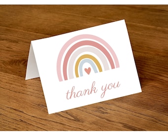 May include: A white card with a pink, yellow, and blue rainbow with a small pink heart in the center. The text "thank you" is written in cursive below the rainbow.