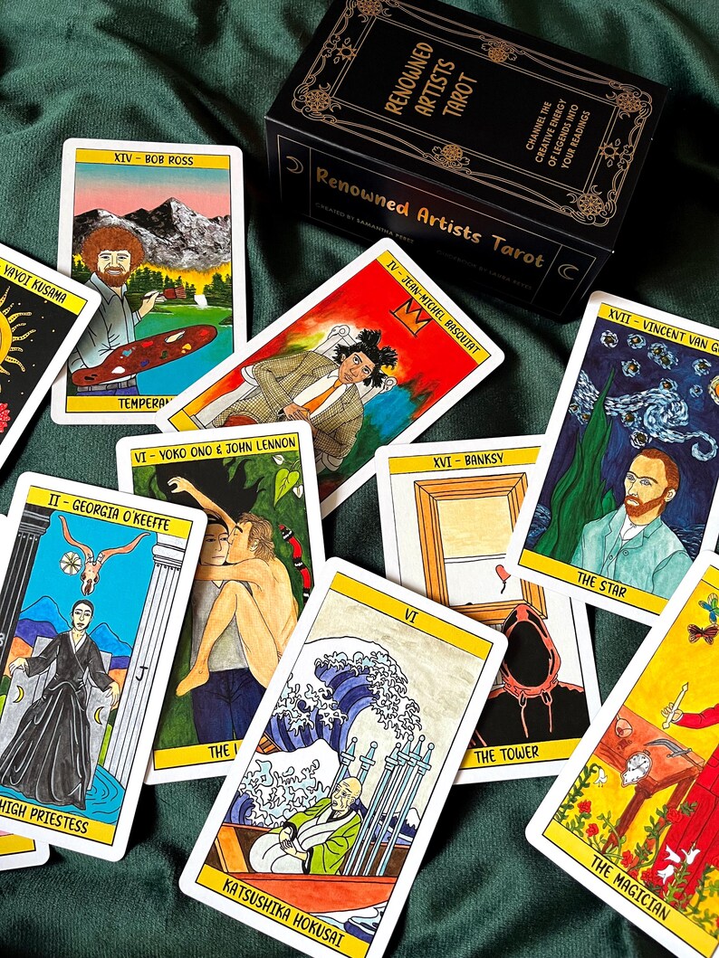 May include: A tarot card deck with the title "Renowned Artists Tarot" on the box. The cards feature illustrations of famous artists like Bob Ross, Jean-Michel Basquiat, and Vincent van Gogh. The cards are on a green surface.
