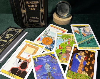 May include: A tarot card deck titled "Renowned Artists Tarot" with a black box and gold lettering. The deck includes several illustrated cards featuring artwork by various artists. A crystal ball sits on a wooden base, and a guidebook is also present.