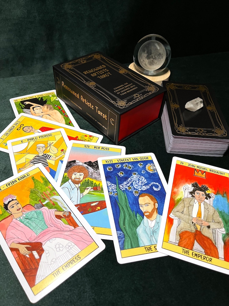 May include: A tarot card deck titled "Renowned Artists Tarot" with a black box and gold lettering. Several tarot cards are fanned out, featuring illustrations of famous artists like Frida Kahlo and Vincent van Gogh. A crystal ball and a quartz crystal are also present.