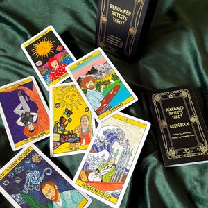 May include: A tarot card deck and guidebook with the text "Renowned Artists Tarot". The cards feature artwork inspired by famous artists like Van Gogh and Hokusai. The box and guidebook are black with gold accents, and the cards are displayed on a green fabric.