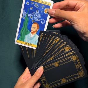 May include: A tarot card featuring Vincent Van Gogh's painting "The Starry Night" with the text "XVII - Vincent Van Gogh" and "THE STAR". The card is held above a fanned deck of black cards with gold decorative borders.
