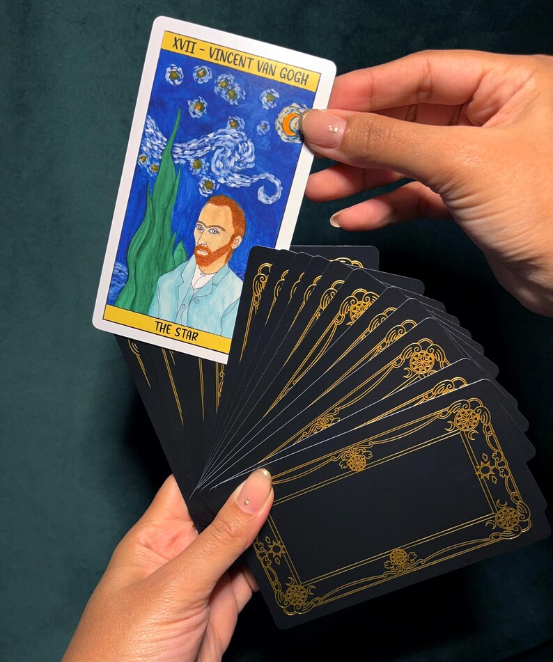 May include: A tarot card featuring Vincent Van Gogh's painting "The Starry Night" with the text "XVII - Vincent Van Gogh" and "THE STAR". The card is held above a fanned deck of black cards with gold decorative borders.