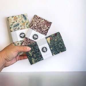 Op de afbeelding: Drie bijenwaswikkelingen met verschillende bloemenpatronen. De wikkelingen zijn gelabeld "Lou Bees Wraps" en bevatten de tekst "The Mighty Tiny".