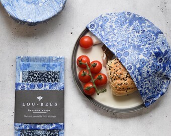 May include: Blue and white floral beeswax wraps by Lou-Bees. The reusable food wraps are shown covering a plate of food and in a stack. The wraps are made of natural, reusable food storage.
