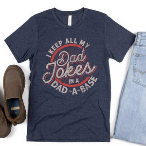 May include: A navy blue t-shirt with a distressed red circle graphic that says "I keep all my Dad Jokes in a Dad-A-Base".