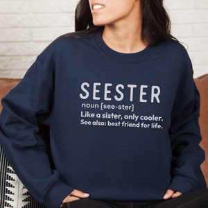 以下が含まれることがあります： 白文字で「SEESTER」と書かれたネイビーブルーのスウェットシャツ。「SEESTER」は「姉妹のようなもの、ただもっとクール。また、親友」と定義されています。