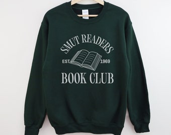 Puede incluir: Una sudadera verde oscuro con el texto "SMUT READERS BOOK CLUB" en blanco. El texto está en forma de arco con un gráfico de libro en el centro. El texto "EST 1969" está debajo del gráfico del libro.