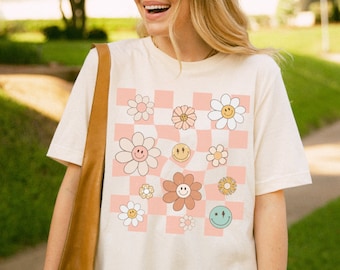 May include: A white t-shirt with a pink and white checkered pattern featuring colourful flowers and smiley faces.