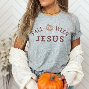 May include: A grey t-shirt with the text "Fall-Ween Jesus" and a small pumpkin graphic. The shirt is being worn by a person holding a small orange pumpkin.