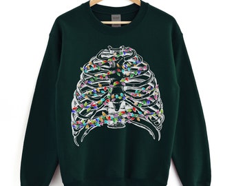 Puede incluir: Una sudadera verde oscuro con un diseño de caja torácica blanca decorada con luces de Navidad de colores.