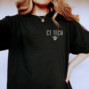 Könnte beinhalten: Schwarzes T-Shirt mit dem Text "CT TECH" und einer Skeletthand, die ein Shaka-Zeichen macht.