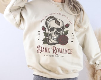 May include: A cream colored sweatshirt with a graphic design of a skull with a snake wrapped around it. The text "Always Falling for the Villain" is above the skull and "Dark Romance Readers Society" is below the skull. There are roses and hearts around the skull.