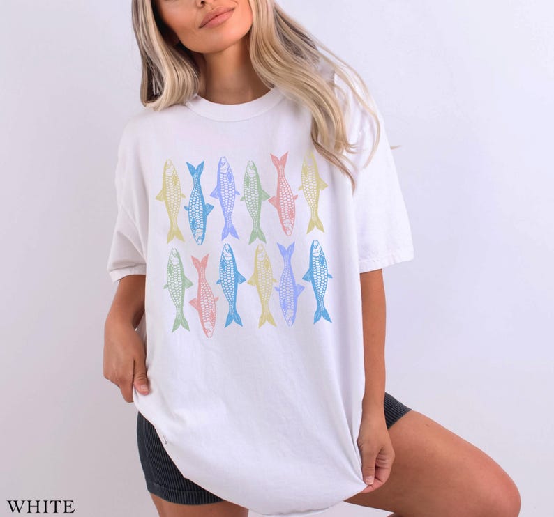 May include: White oversized t-shirt with a colorful fish pattern. The fish are in a variety of pastel colors, including blue, green, yellow, and pink.